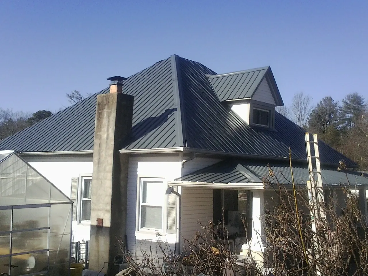 Dark blue standing seam metal roof on a white farmhouse with dormer — Slate & Tile Roof Repair by Roofing Brothers in Willards