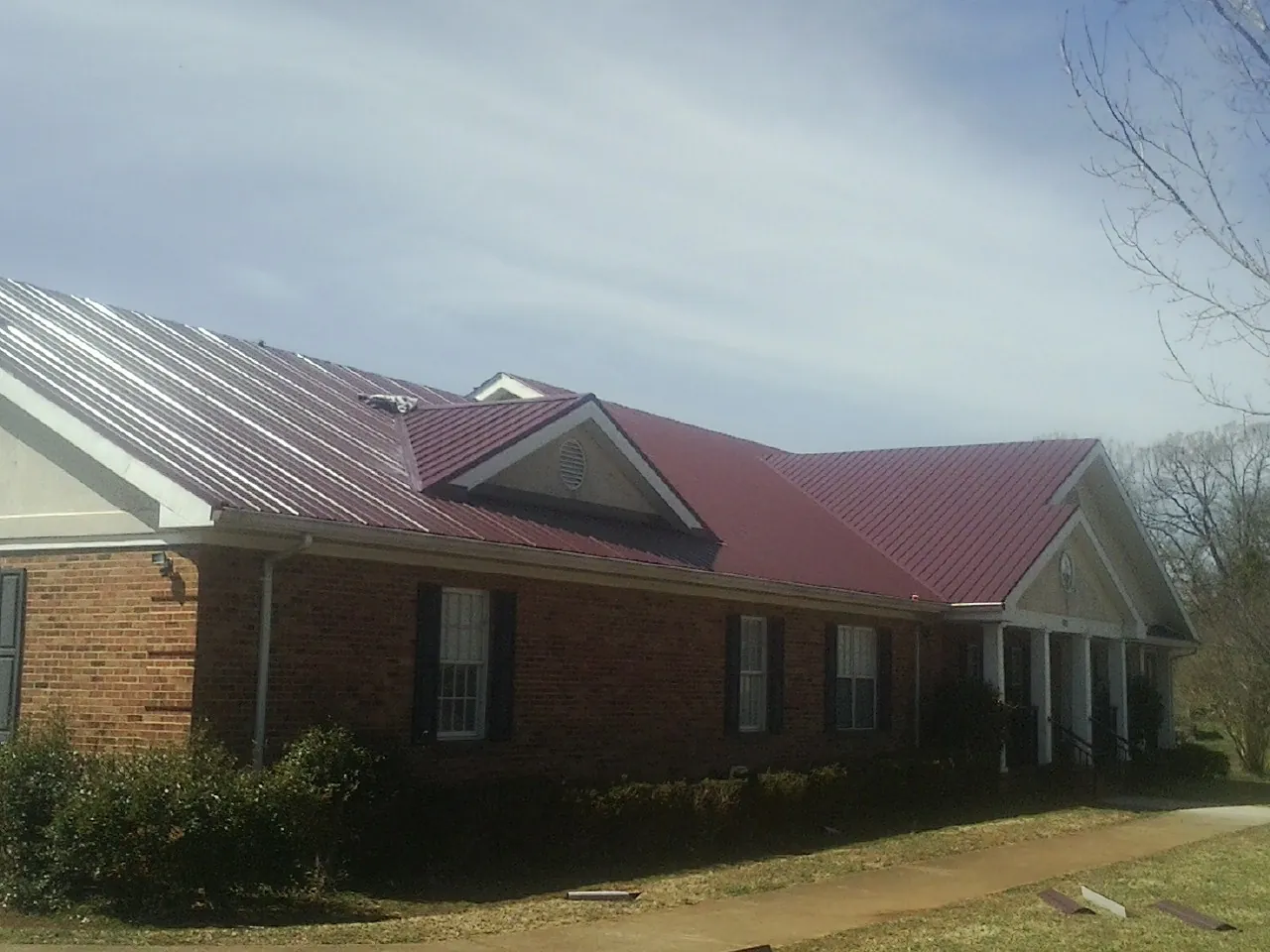 Red metal roof with gabled entries on a long brick building, from a Hail Damage Roof Repair job in Willards