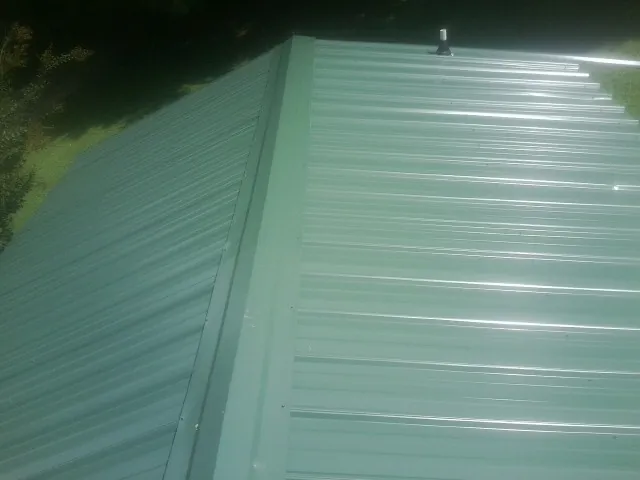 New green metal panels meeting at the ridge of a roof — Flat Roof Repair work by our crew in Willards