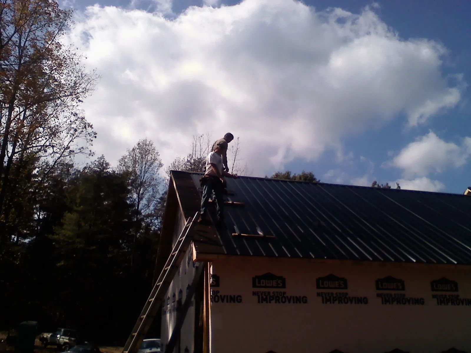 Roofer fastening dark metal panels high against a cloudy sky, from a Roof Inspection job in Willards