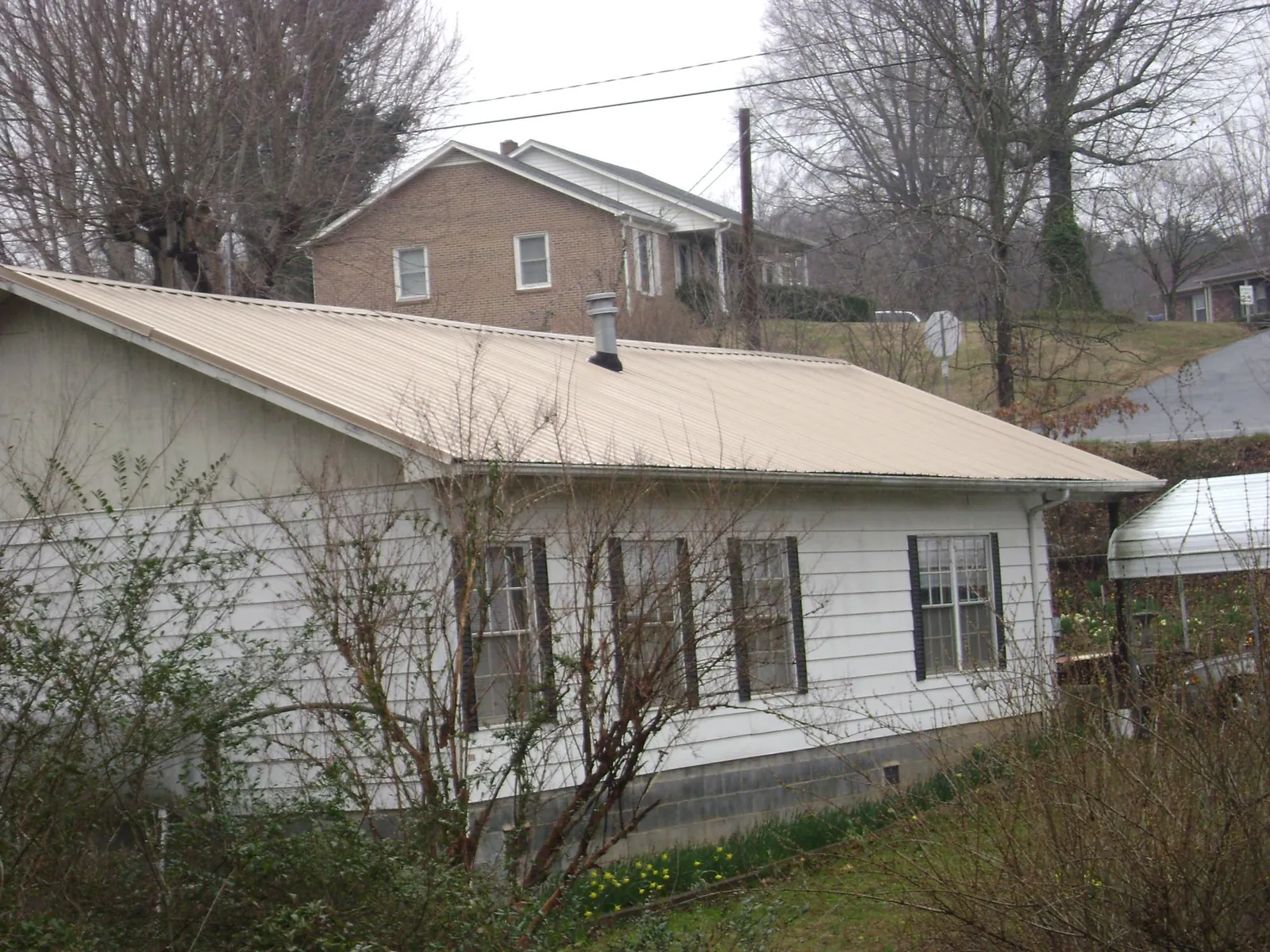 Tan metal roof on a white sided house set into a hillside — Commercial Roofing by Roofing Brothers in Willards